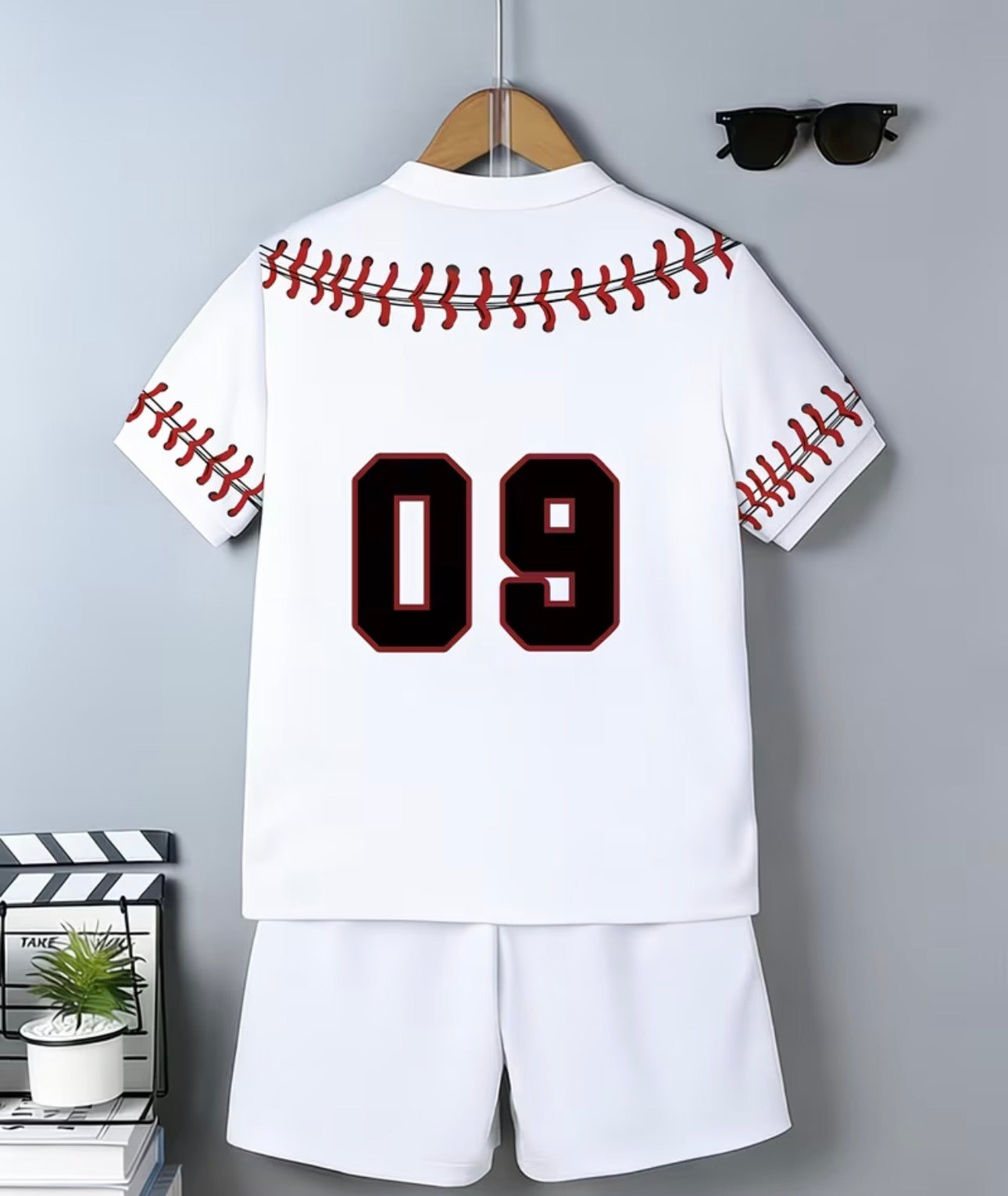 White baseball-themed shirt with red stitching and number 09 on a hanger against a gray wall.