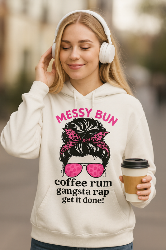 A blonde woman smiling while wearing white headphones and a grey pullover hoodie. The hoodie features a graphic of a messy bun with a pink leopard print bandana and pink sunglasses. Above and below the graphic is the text in hot pink and black: 'MESSY BUN COFFEE RUM GANGSTA RAP GET IT DONE!'. She is holding a takeaway coffee cup.