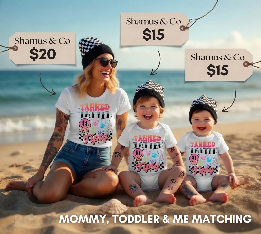 Woman and two children sitting on a beach wearing matching 'Tanned Tatted Tipsy' shirts with product tags displayed.