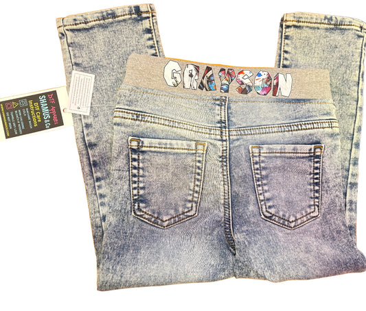 Folded toddler jeans with personalized name ‘GRAY’ on a gray waistband, displayed on an orange background.